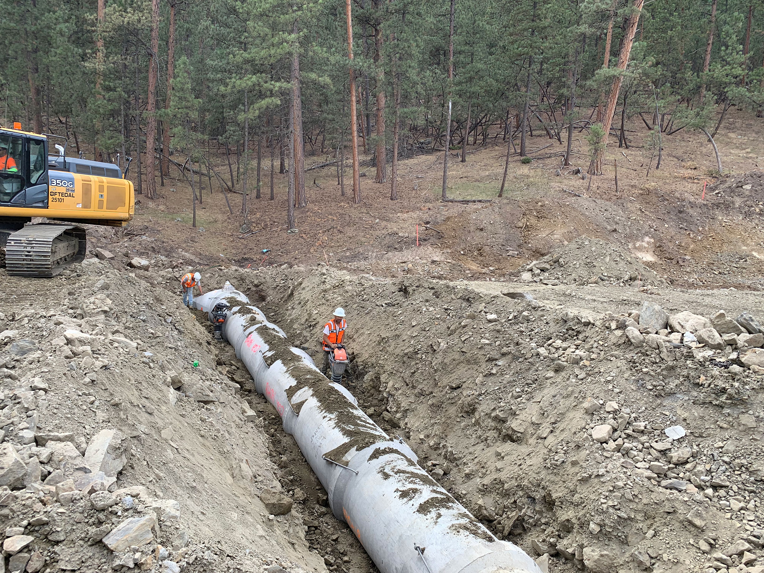 Construction workers working on pipe in ground.
